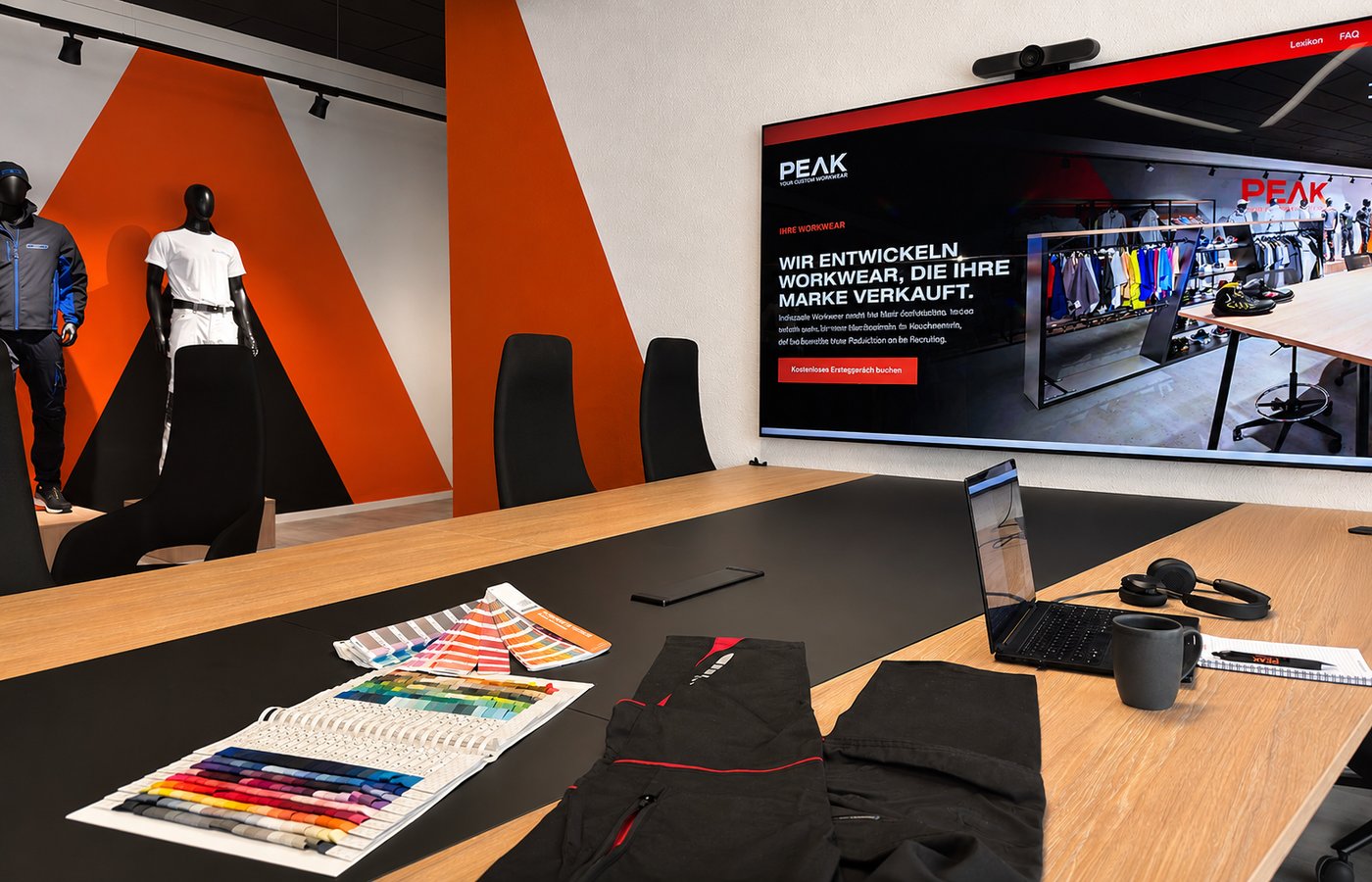 Foto vom PEAK Konferenztisch mit Farbfächern und Hose und TV im Hintergrund